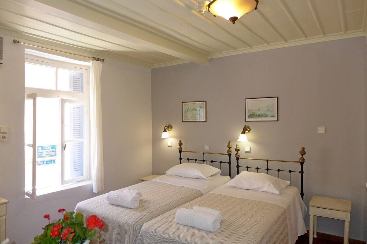 A hotel room with two beds, a window with curtains, a small bedside table, and wall-mounted lamps.