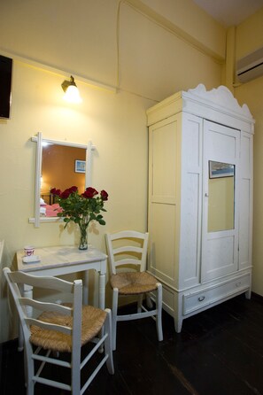 Una habitación con un armario blanco, una mesita con un jarrón de rosas rojas y dos sillas de mimbre.