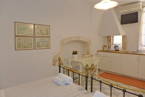 Una habitación con una cama, un escritorio con una silla, una mesita con una planta y una ventana con cortinas.