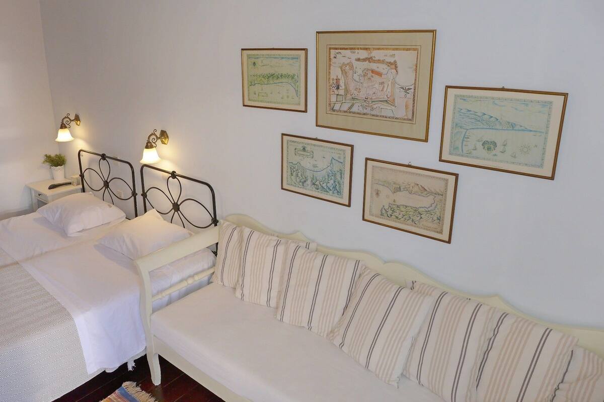 A bedroom with two beds, a white sofa, and framed artwork on the wall.