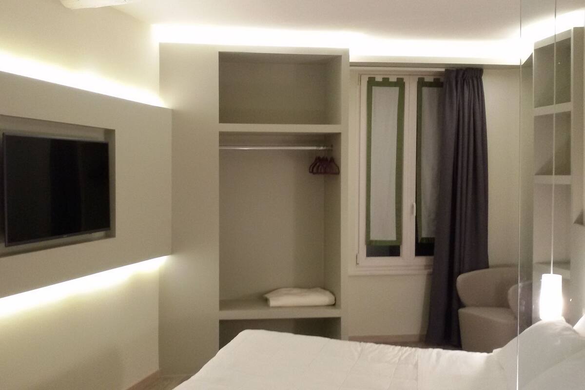 Une chambre d’hôtel avec un lit, un téléviseur fixé au mur, une armoire et une fenêtre avec des rideaux.