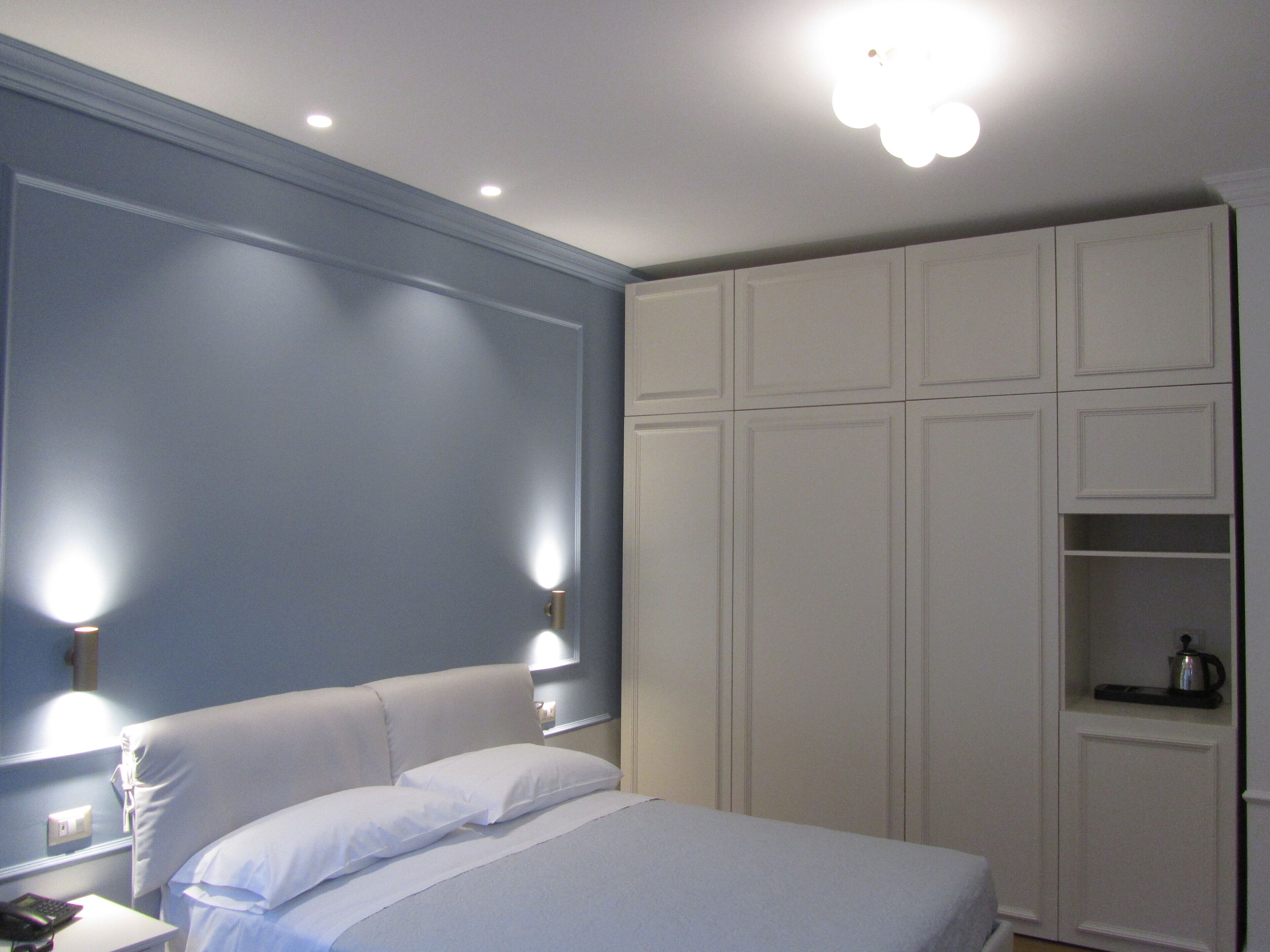A bedroom with a bed, bedside lamps, a wardrobe, and a nightstand with a phone and charger.