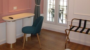 A room with a teal chair, a small white table with a remote control, a window with a curtain, and a metal rack. - Hotel Borgovico (Como)