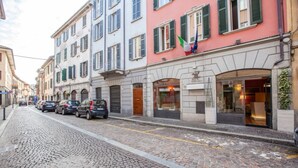A cobblestone street lined with multi-story buildings, some with shops on the ground floor. - Hotel Borgovico (Como)