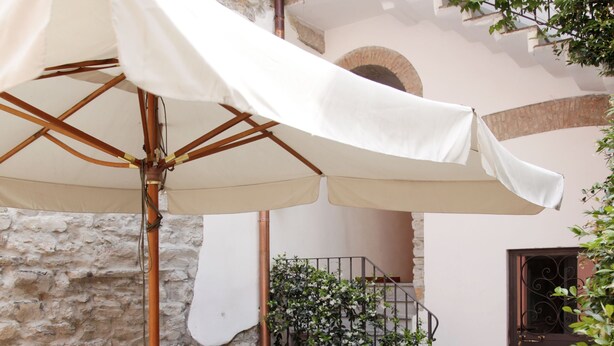 An outdoor patio with a table and chairs under a white umbrella, a staircase, and a stone wall. - Hotel Borgovico (Como)
