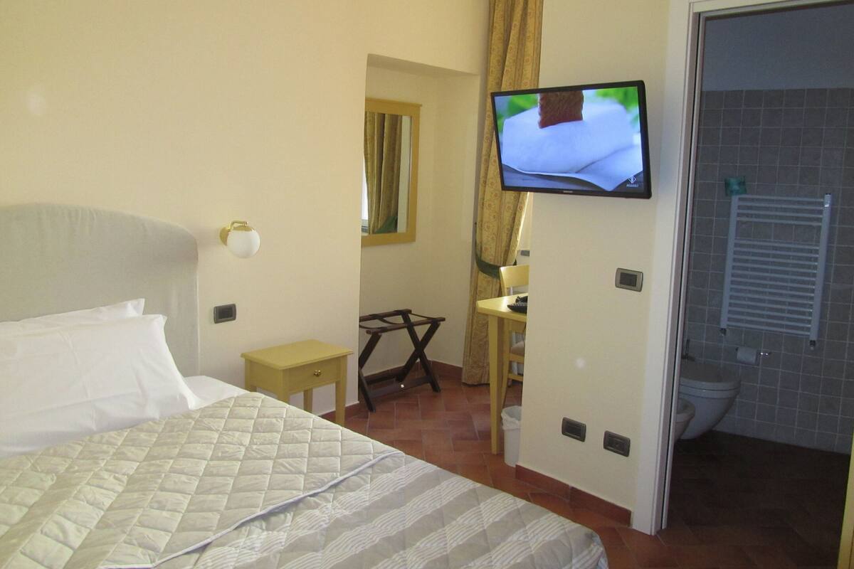 Une chambre d’hôtel comprenant un lit, un téléviseur fixé au mur, une petite table et une porte donnant accès à une salle de bain.