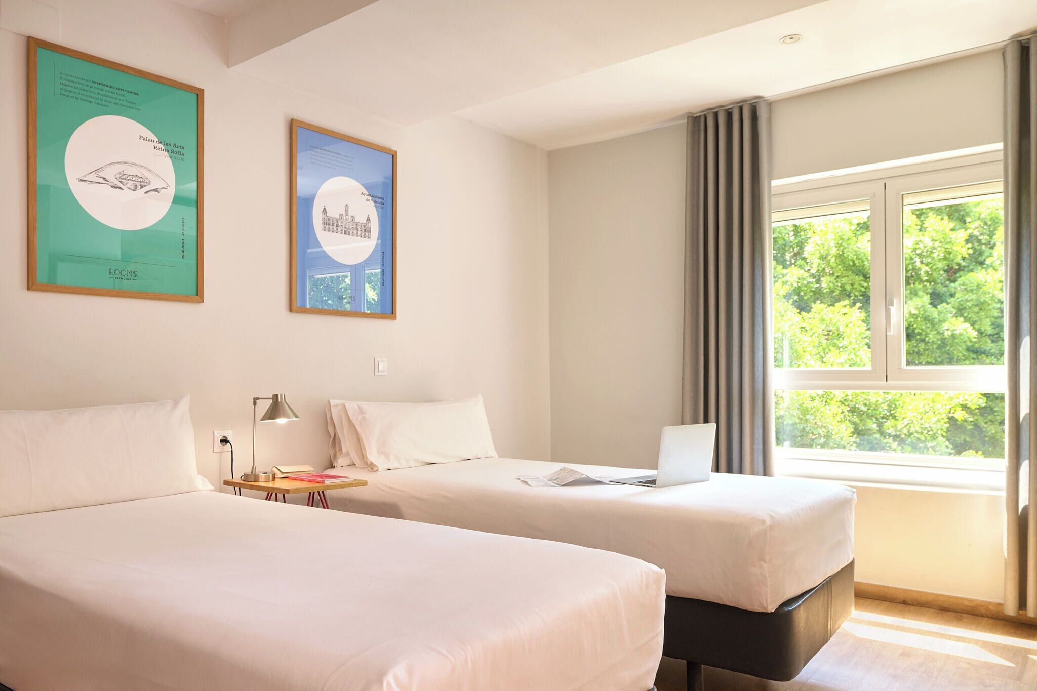 Een hotelkamer met twee bedden, een bureau met een laptop en een raam met gordijnen.