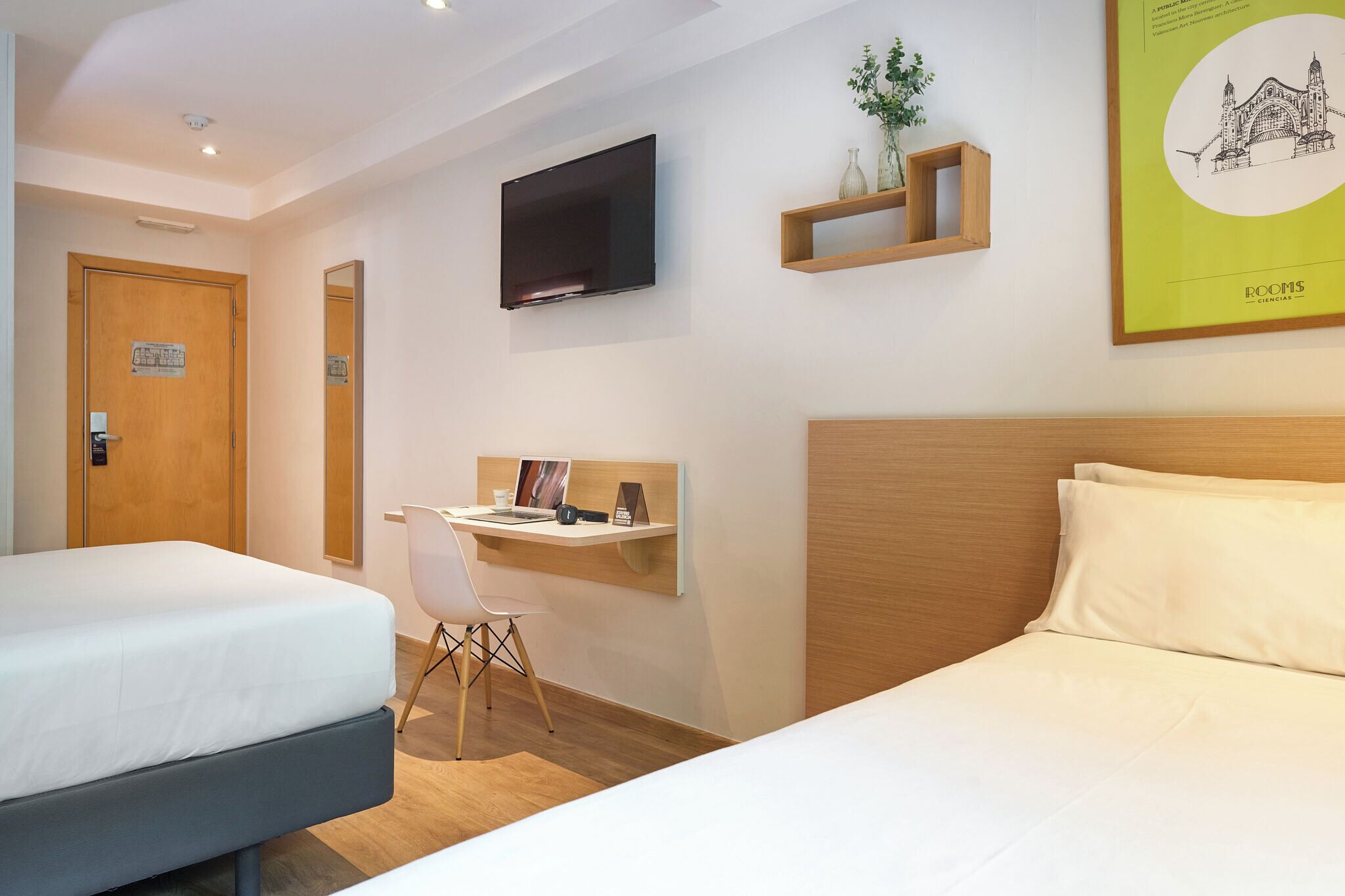 Une chambre d’hôtel avec deux lits, un bureau, une chaise, une télévision et un tableau encadré au mur.