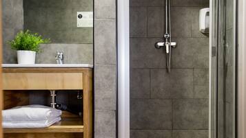 A modern bathroom with a glass shower enclosure, a wooden vanity, and a potted plant.