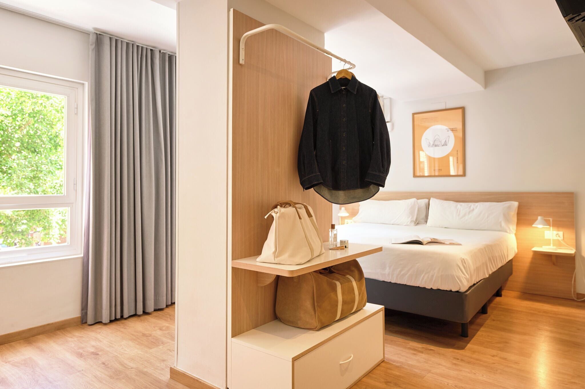 A modern bedroom with a bed, bedside table, lamp, and a hanging coat rack.