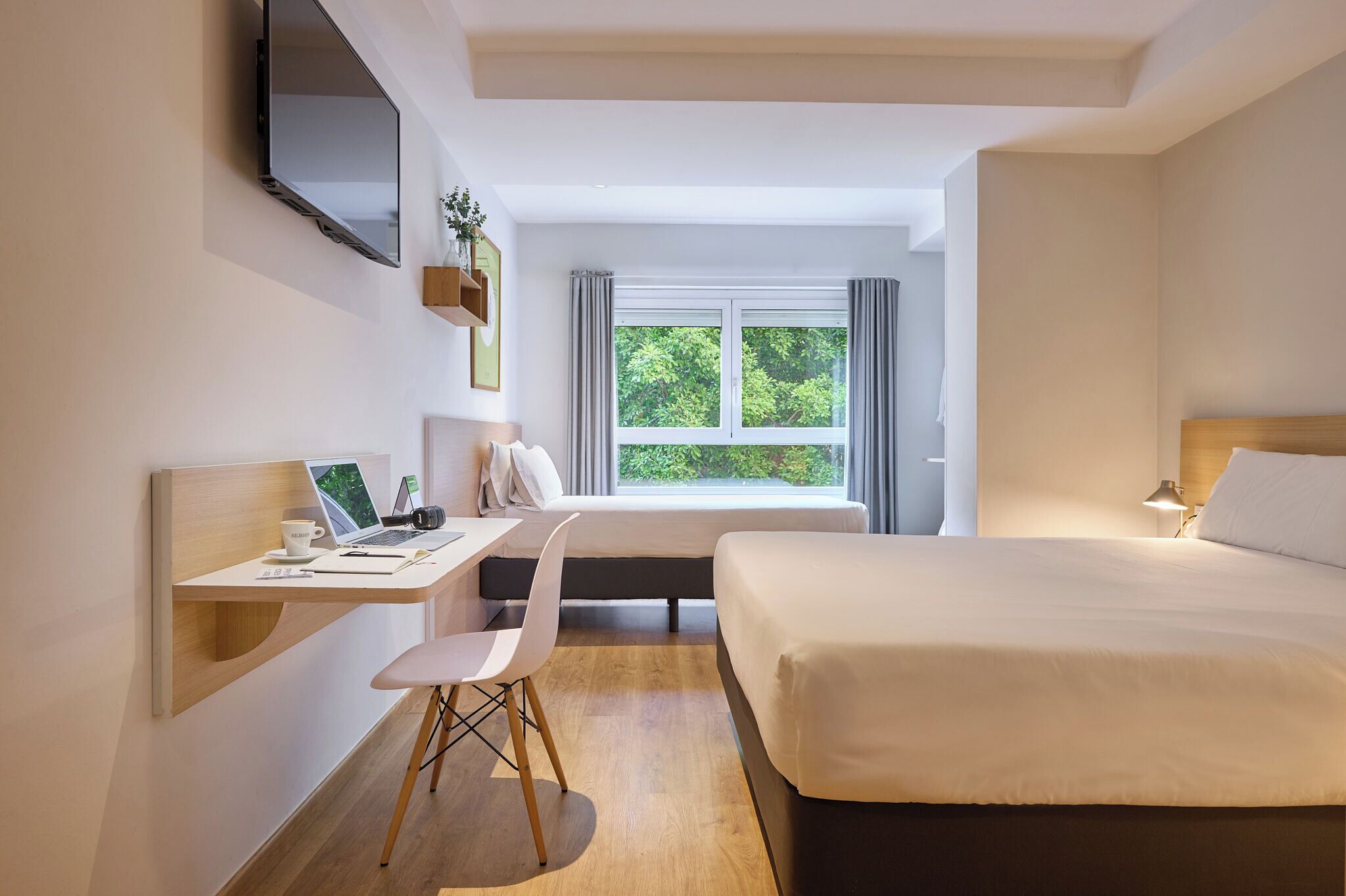 Una habitación de hotel moderna con cama, escritorio, silla y un amplio ventanal con cortinas.