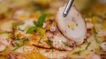 Primer plano de un plato con tentáculos de pulpo, hierbas y salsa.