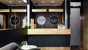 A reception area with a modern design, featuring a reception desk, a waiting area with a sofa, and a wall with circular signs indicating different services. - Rooms Ciencias (Valencia)