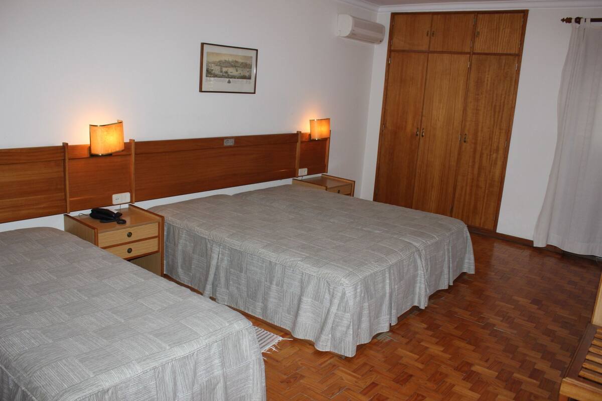 Habitación de hotel con dos camas, cabeceros de madera, mesitas de noche con lámparas, un armario y un cuadro en la pared.