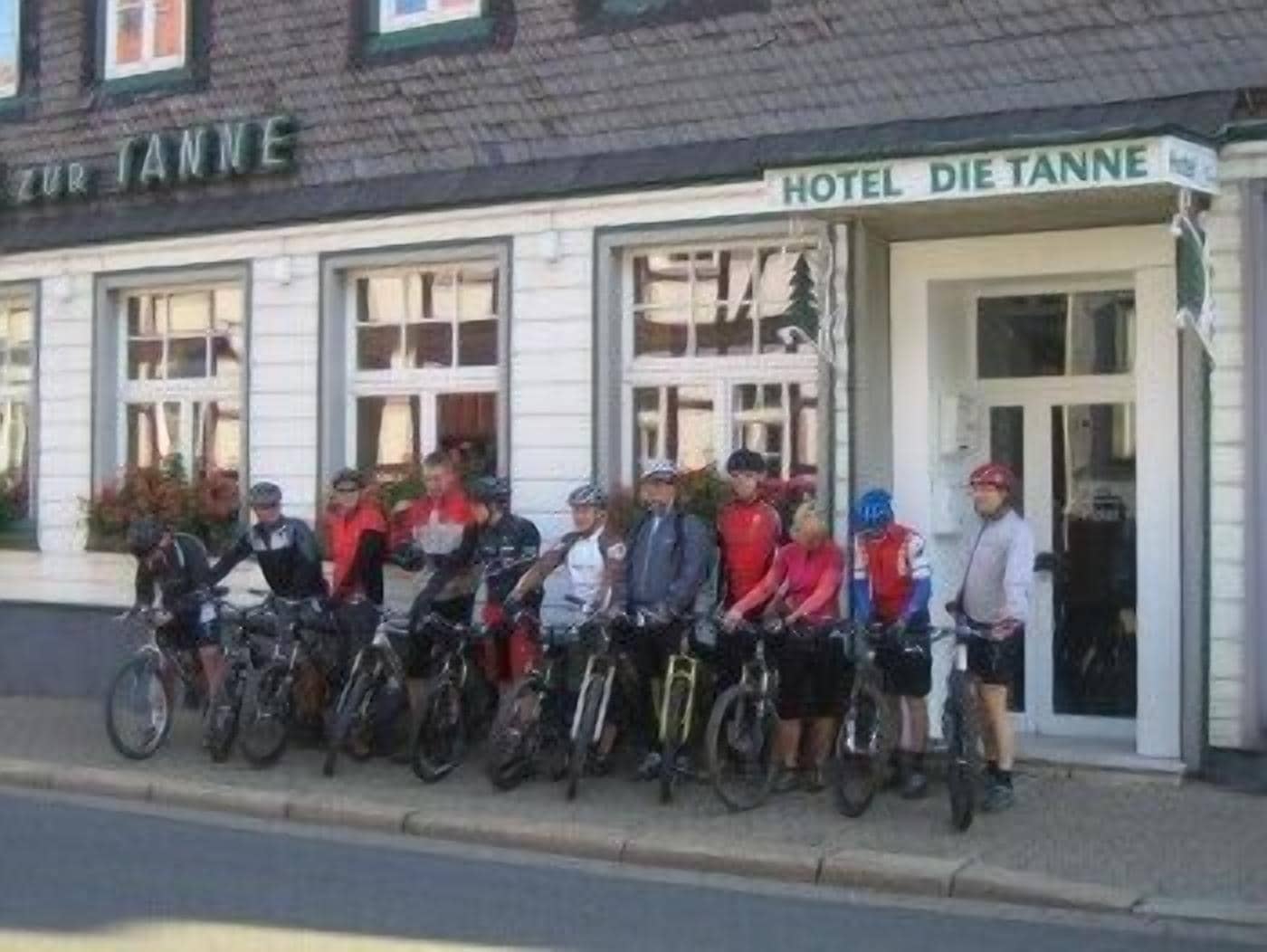 Ein Hotel namens "HOTEL DIE TANNE", vor dem eine Radsportlergruppe steht.