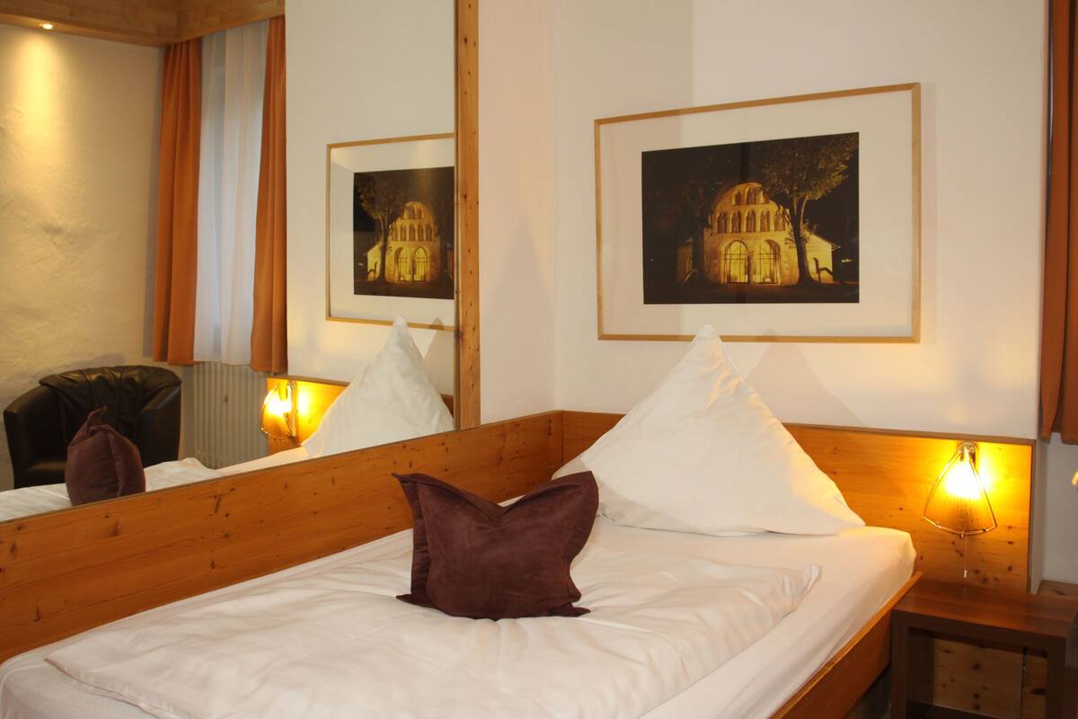 A neatly made bed with white linens and a brown pillow, a wooden headboard, and a nightstand with a lamp.