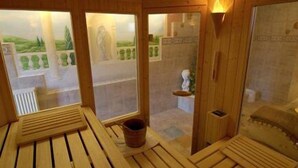 Ein Saunaraum mit Holzbänken, einem kleinen Eimer und einem an der Wand befestigten Ablagebrett.