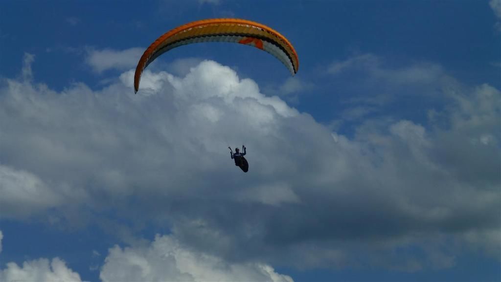 A paraglider with a colorful canopy flying against a backdrop of clouds.