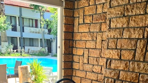 A dining table set with various dishes, including watermelon, cheese, and olives, in a room with a stone wall and a view of a swimming pool.