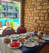 Una mesa de comedor servida con varios platos, incluyendo sandía, queso y aceitunas, en una habitación con pared de piedra y vista a una piscina.