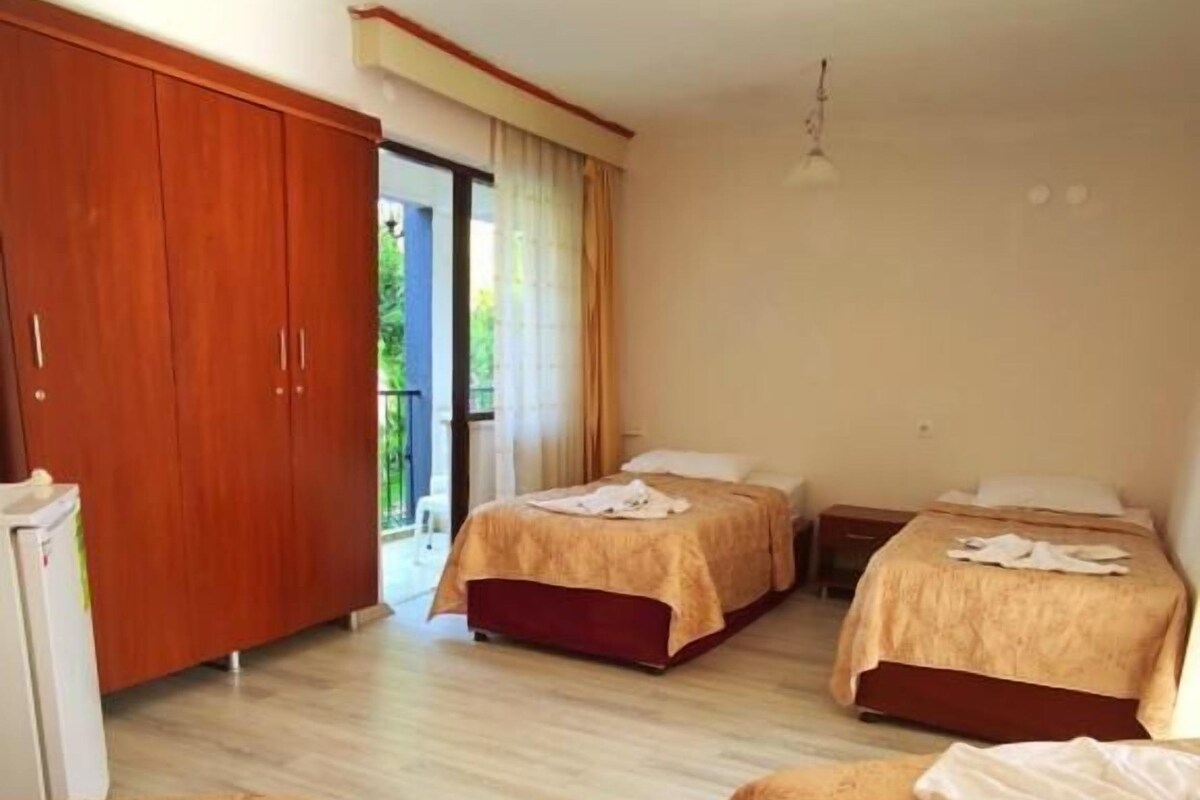Habitación de hotel con tres camas, un armario y vistas al exterior.