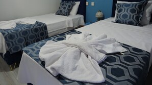A hotel room with two beds, each with a patterned bedspread and matching pillows. A white bathrobe is draped over the bed in the foreground.