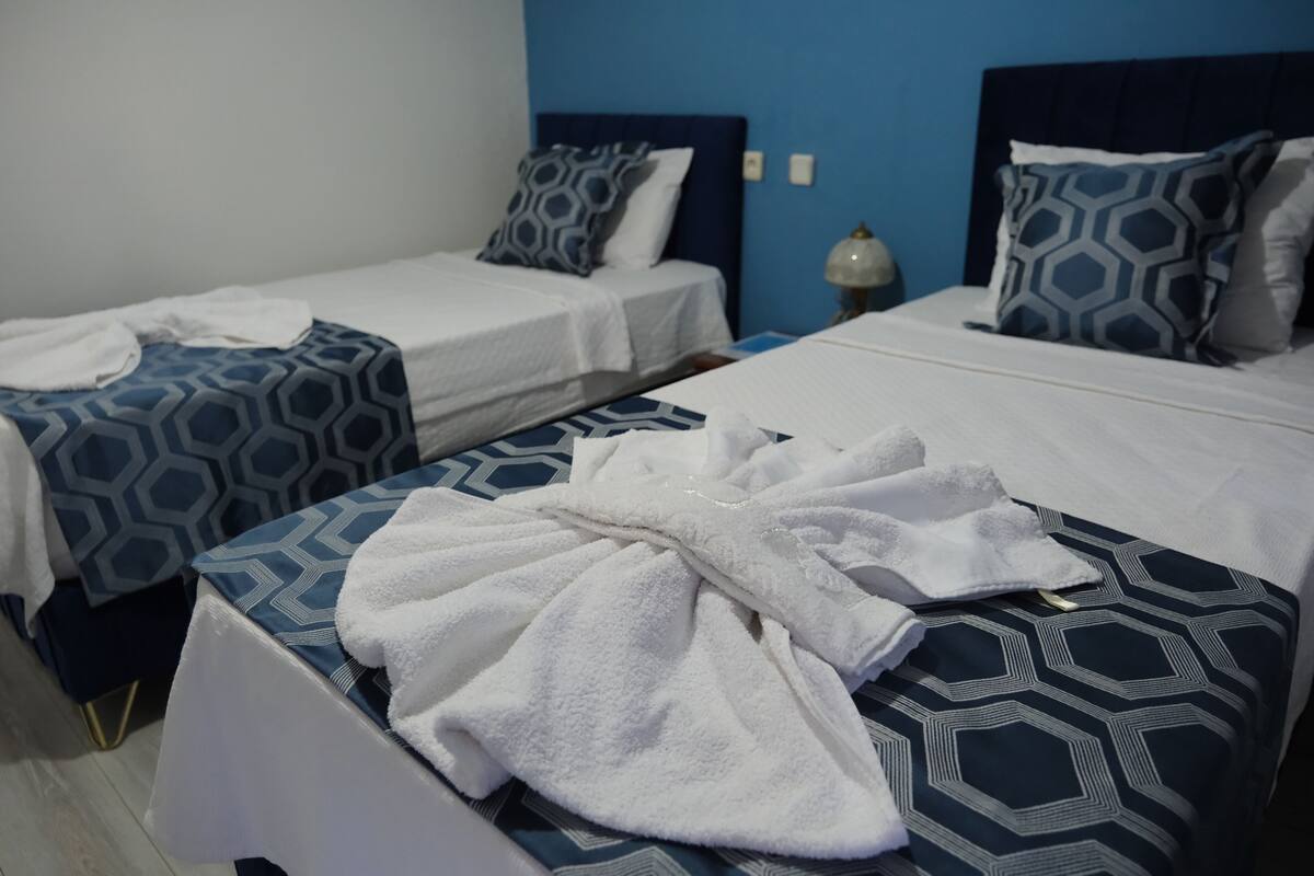Une chambre d’hôtel avec deux lits, chacun recouvert d’une couvre-lit à motifs et agrémenté d’oreillers assortis. Un peignoir blanc est posé sur le lit, au premier plan.