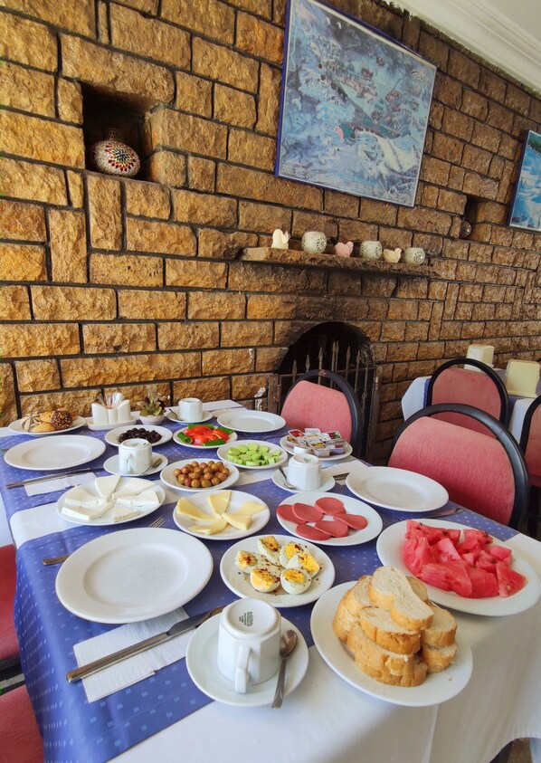 Une table à manger dressée avec divers plats, notamment du fromage, des œufs et du pain, dans une pièce dont le mur est en briques et qui possède une cheminée.