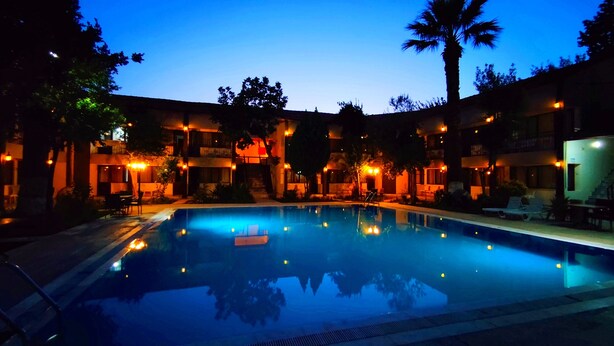 A swimming pool surrounded by buildings with outdoor seating and palm trees.