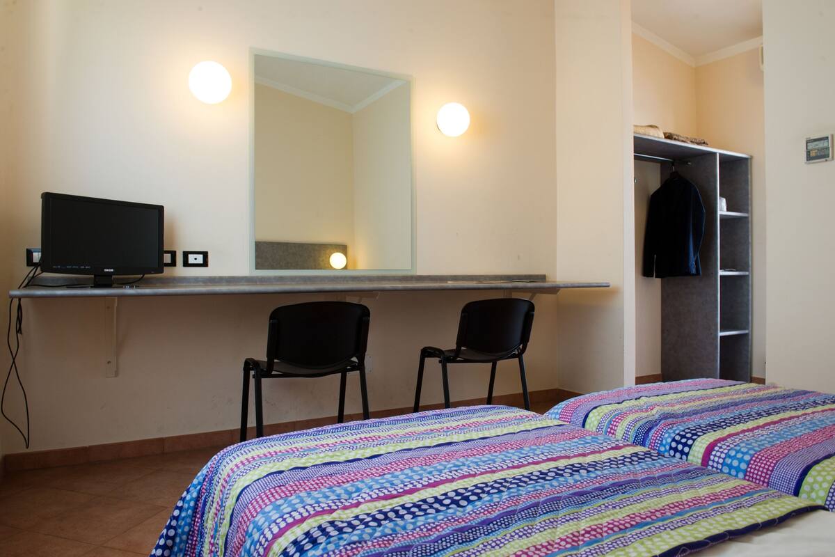 A bedroom with a bed, a desk with a computer, two chairs, a mirror, and a wardrobe.