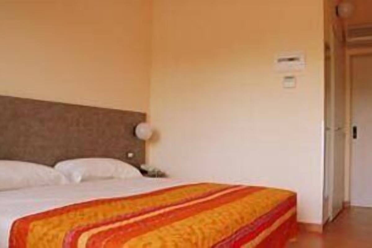 A hotel room with a bed, a nightstand, a lamp, and a door.