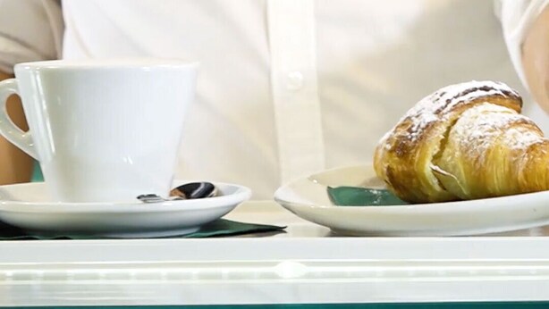 Una persona sentada a una mesa con una taza blanca y un plato con un pastel.