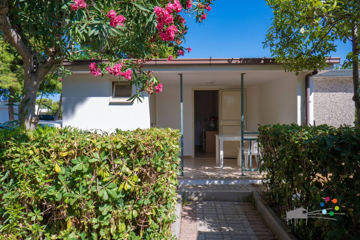 Ein zweistöckiges Haus mit überdachter Veranda, kleinem Balkon und einem Garten mit blühenden Pflanzen.