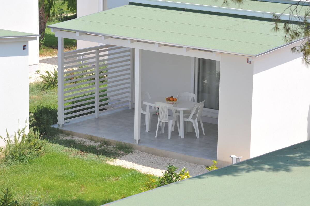 Ein überdachter Außenbereich mit Tisch und Stühlen, einer Obstkorb und eine kleine Gartenanlage.