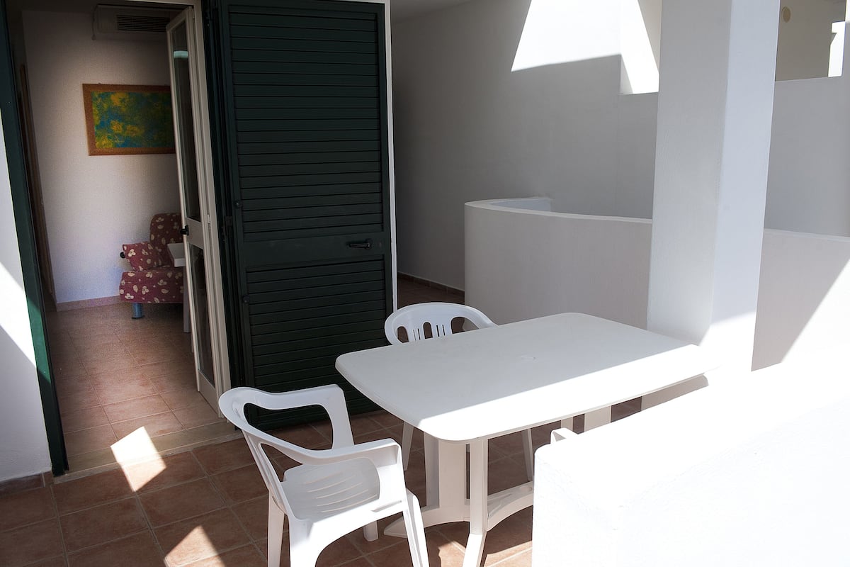 Ein kleiner Patio-Bereich mit weißem Tisch und Stühlen, einer grünen Tür und einem Fliesenboden.