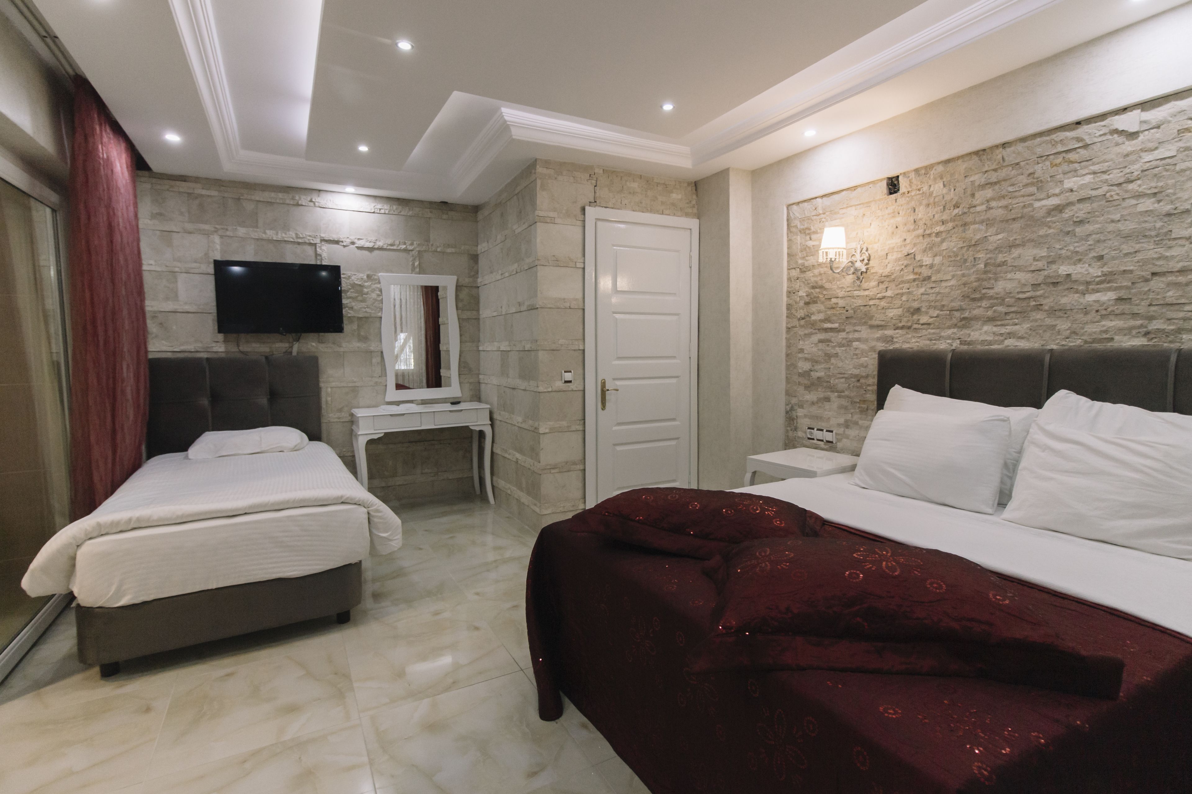 Quarto de hotel com duas camas, televisão, escrivaninha e parede de pedra.