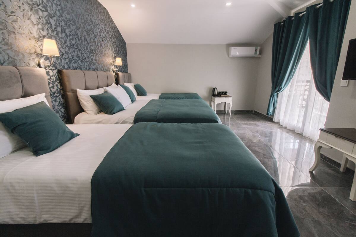 A hotel room with two beds, a small table, a TV, and a window with curtains.