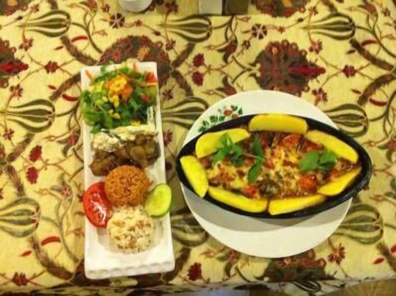 A table with a floral tablecloth, a plate of food including a stuffed eggplant dish, a side salad, and a small bowl of rice.