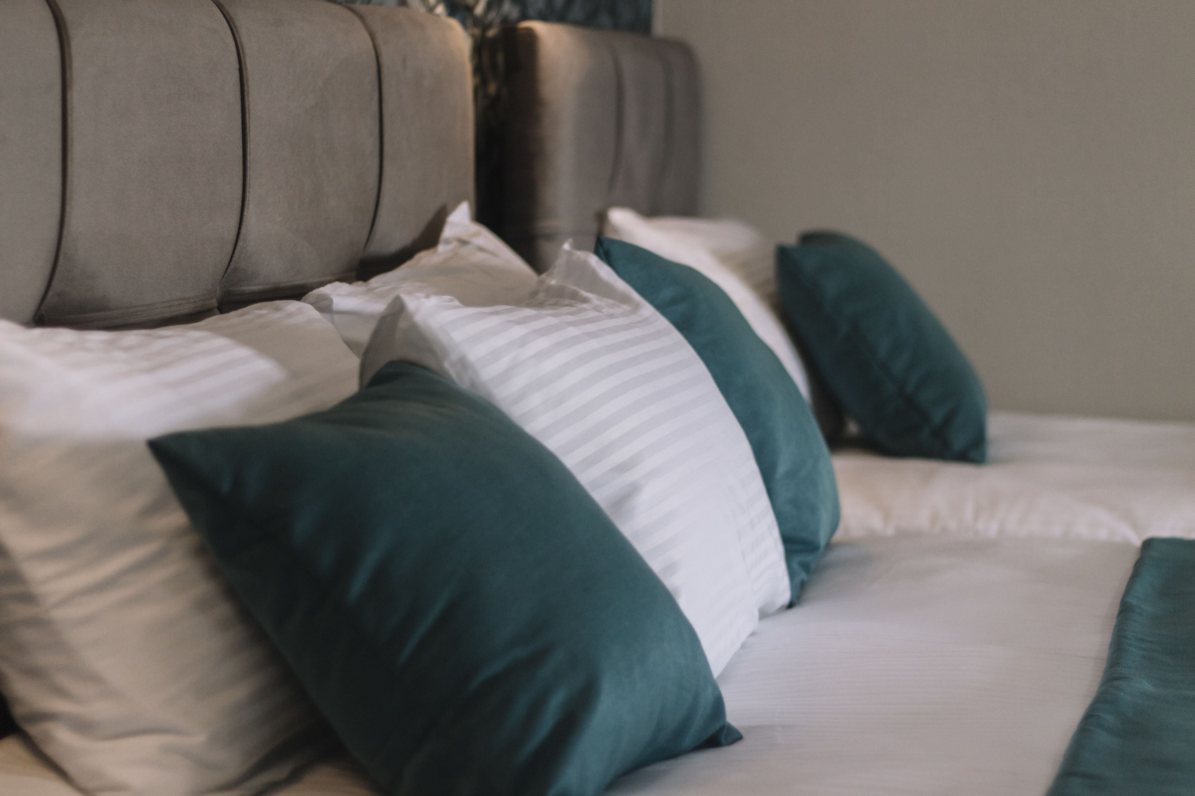 Un letto con una testiera grigia rivestita in tessuto e numerosi cuscini nei toni del verde acqua e del bianco.