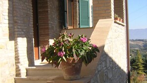 A stone building with a wooden staircase leading to a door with green shutters. A potted plant with pink flowers is placed on the steps. - Residenza del Marchese (Gualdo Cattaneo)