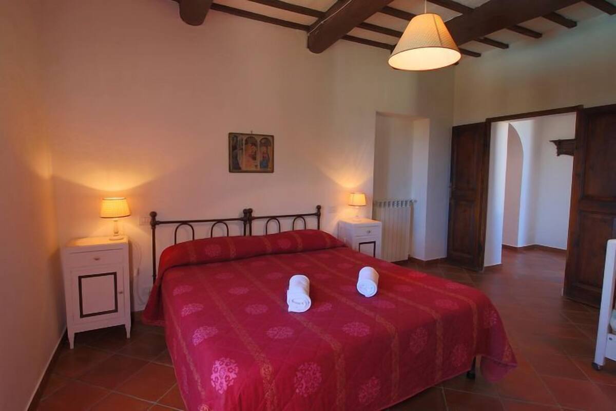 A bedroom with a bed, two bedside tables, a lamp, a radiator, and a door.