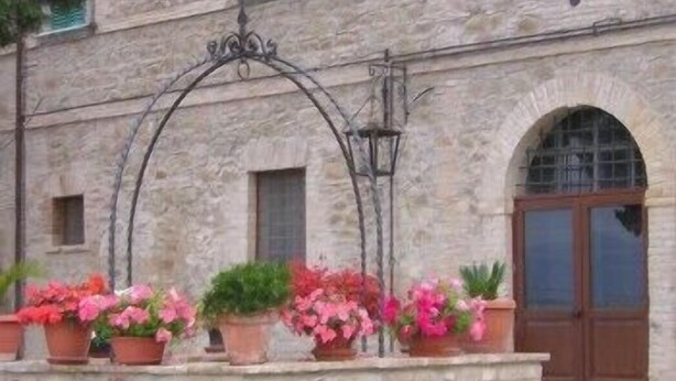 A stone building with a wooden door and a window. There are potted plants on a stone ledge in front of the door. - Residenza del Marchese (Gualdo Cattaneo)