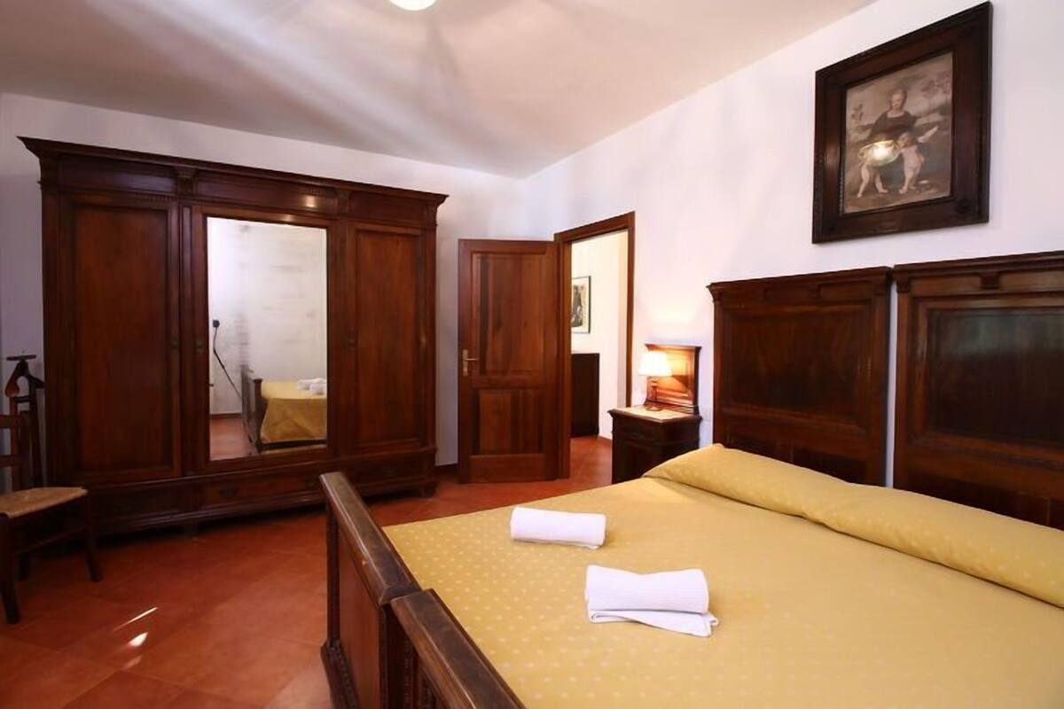 A hotel room with a bed, wooden wardrobe, and a painting on the wall.