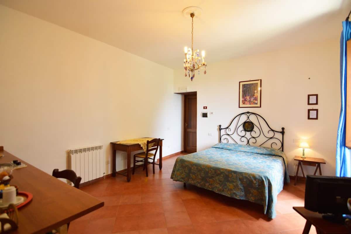 A bedroom with a bed, a desk, a chair, a radiator, and a chandelier.