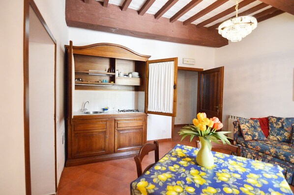 Un comedor con una mesa lista para dos personas, un armario de madera con vajilla y un sofá floral.