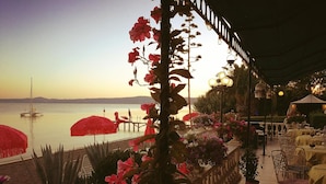 Un espacio de comedor al aire libre con vista al mar, que cuenta con una pérgola adornada con flores, mesas y sillas.