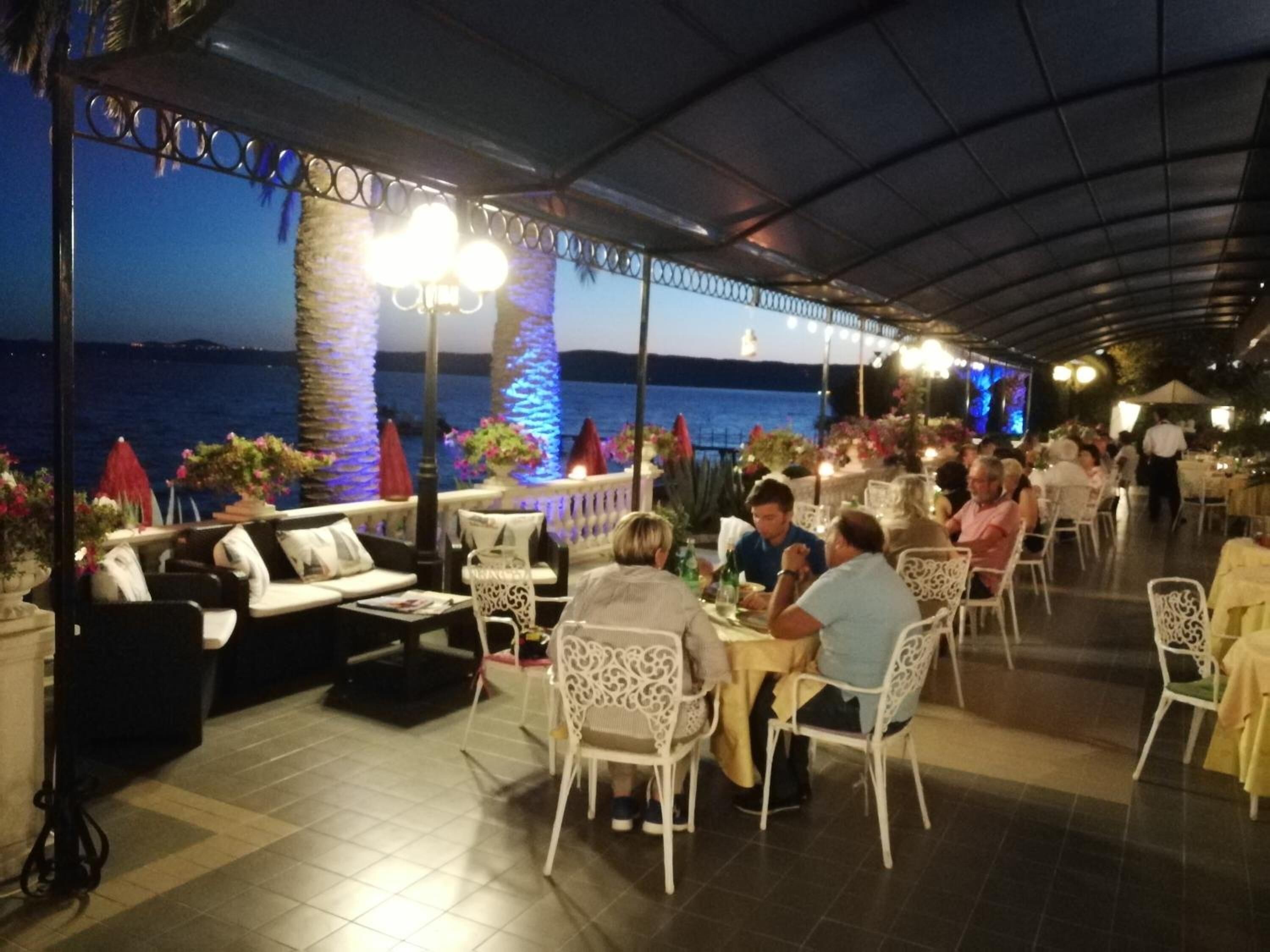 Area pranzo all'aperto con tavoli e sedie, con vista sul mare.
