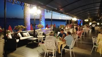 Un espace extérieur aménagé pour les repas, avec des tables et des chaises, offrant une vue sur la mer.