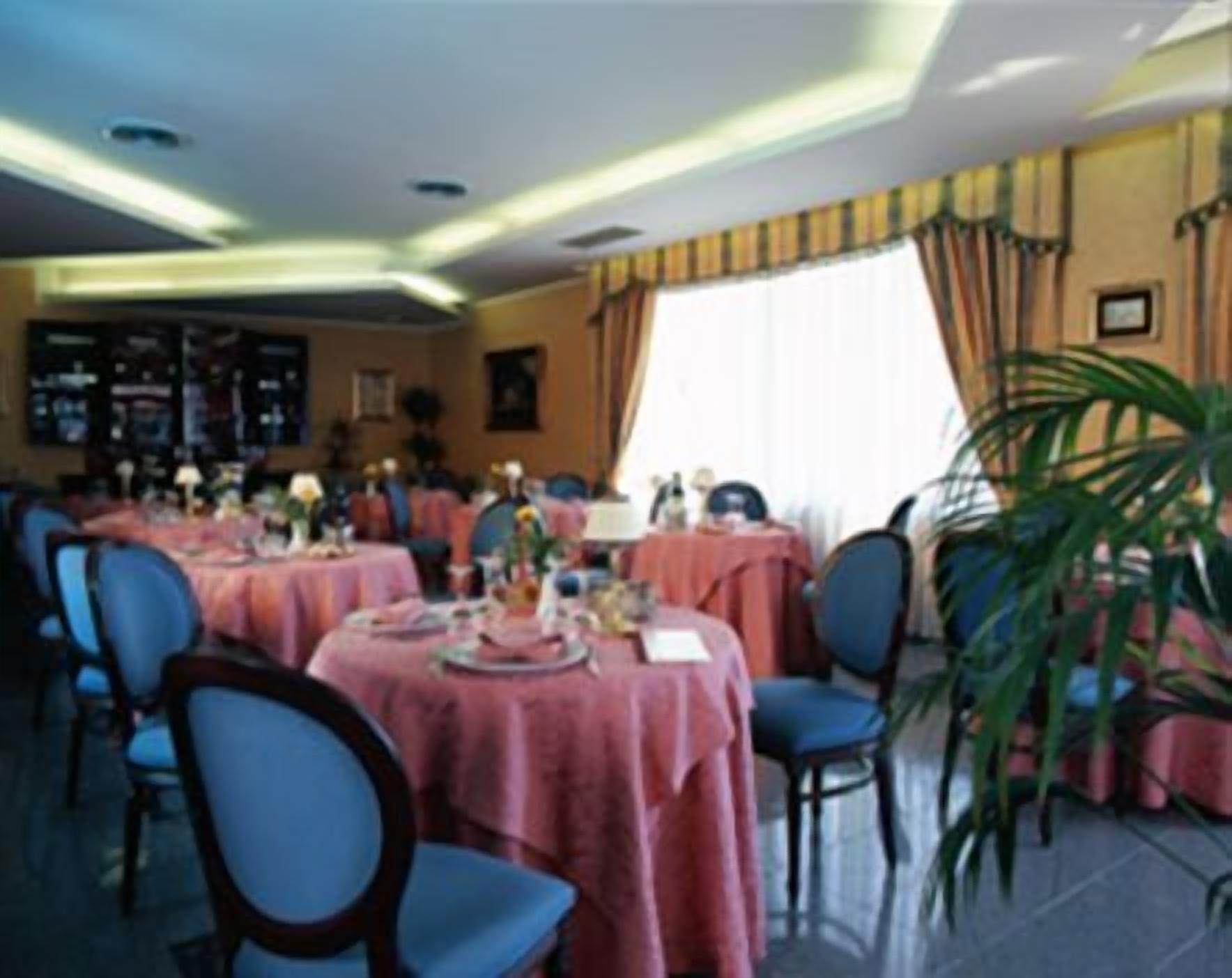 Un comedor con mesas redondas cubiertas con manteles rosa, sillas azules y una planta grande en maceta.