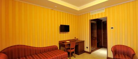 A hotel room with striped yellow walls, a sofa, a desk with a chair, and a television.